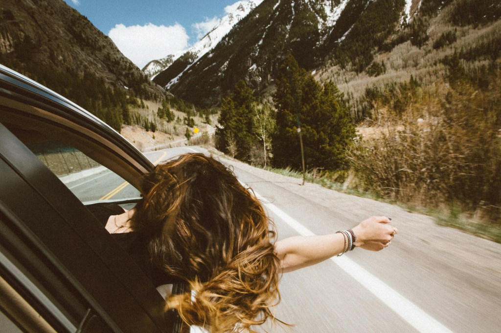 Young female hanging out of passenger side on a drive through mountains.